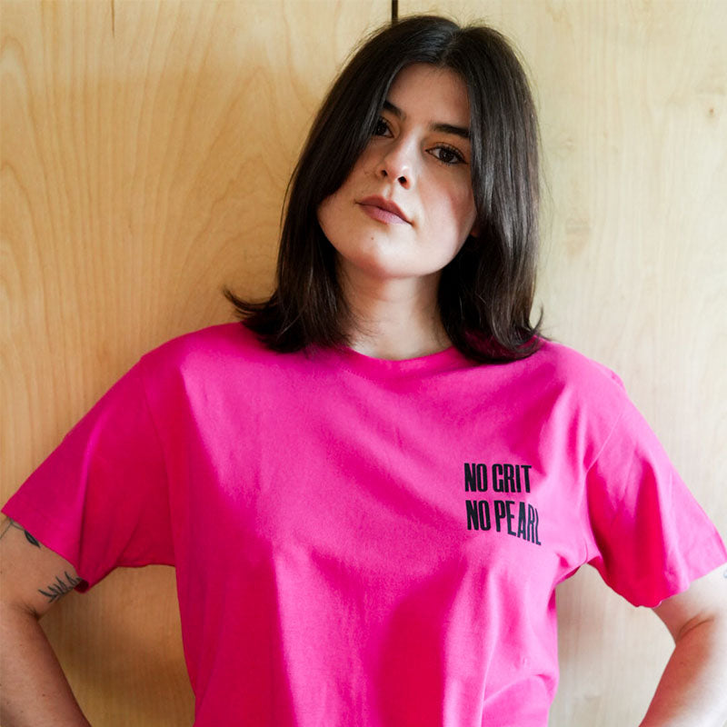A woman wearing a pink T-shirt with the slogan 'No Grit No Pearl'.