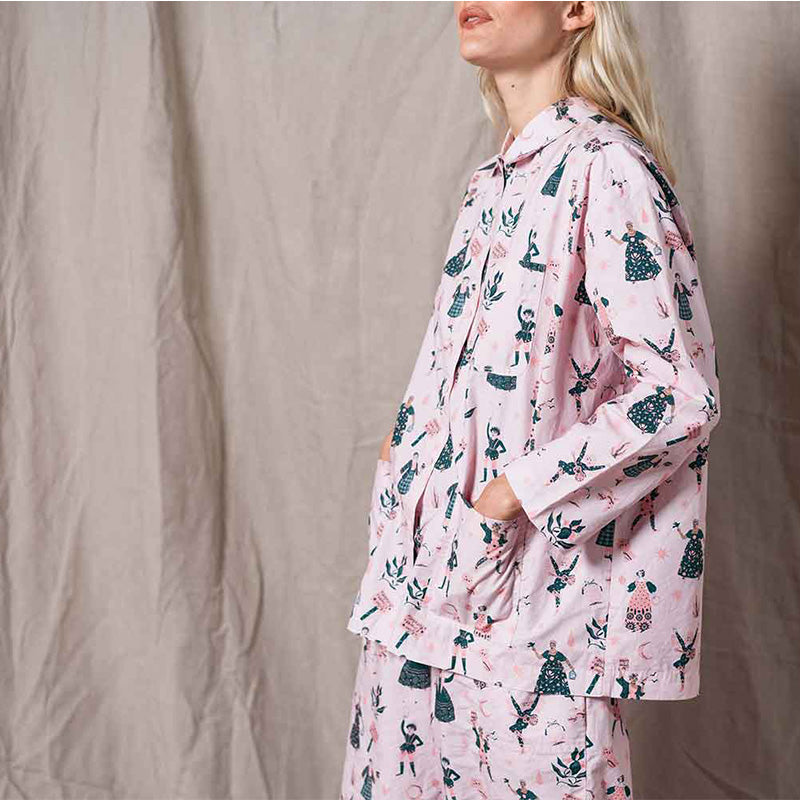 Woman wearing light pink cotton pyjamas with a pattern consisting of illustrations of women.
