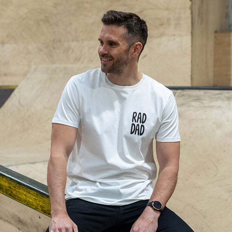 A man with a light beard is wearing a white T-shirt with the slogan 'RAD DAD' clearly visible in bold black type.