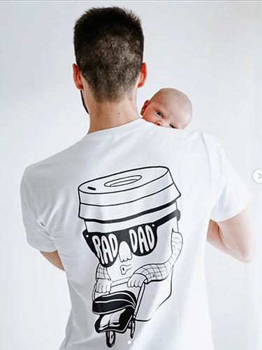 A man with a light beard is wearing a white T-shirt with the slogan 'RAD DAD' clearly visible in bold black type.