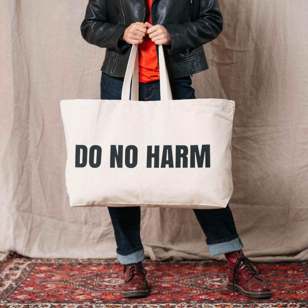 A woman is carrying a tote shopping bag with the phrase 'Do No Harm' clearly visible in bold black type.